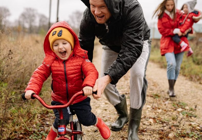 Father helping son ride a bicycle on a fall day while mother and daughter watch.