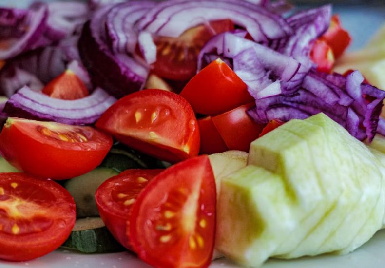 Colorful summer vegetable salad featuring tomatoes, cucumbers, and red onion slices on a plate.